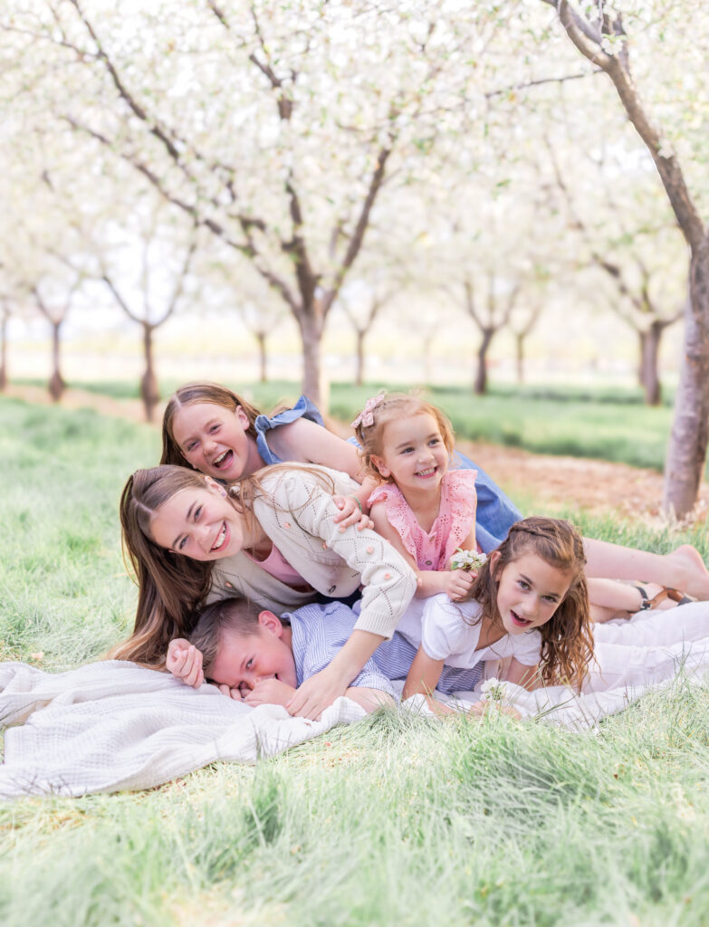 Siblings playing together beneath flowering orchard trees during a spring portrait session in Utah