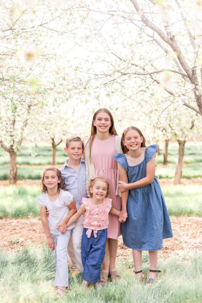 Siblings smiling and posing in a flowering orchard during a spring portrait session in Utah