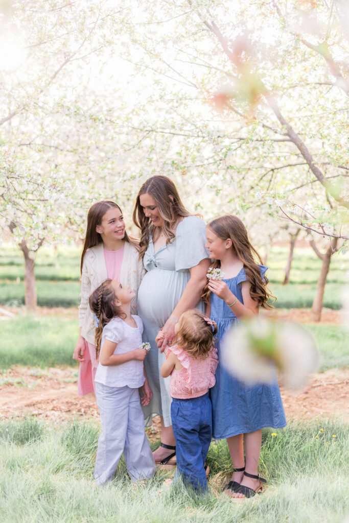 Mother and daughters together in a flowering orchard during a spring family and maternity photo session in Utah County orchard