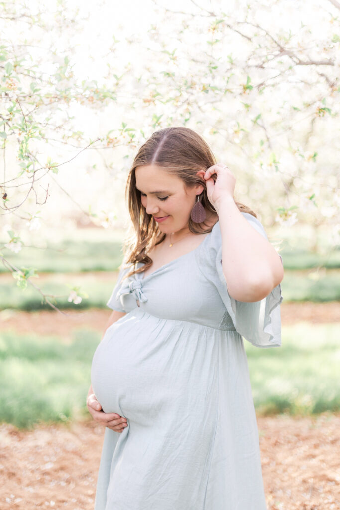Expectant mother standing among flowering orchard trees during a spring maternity photo session in Utah