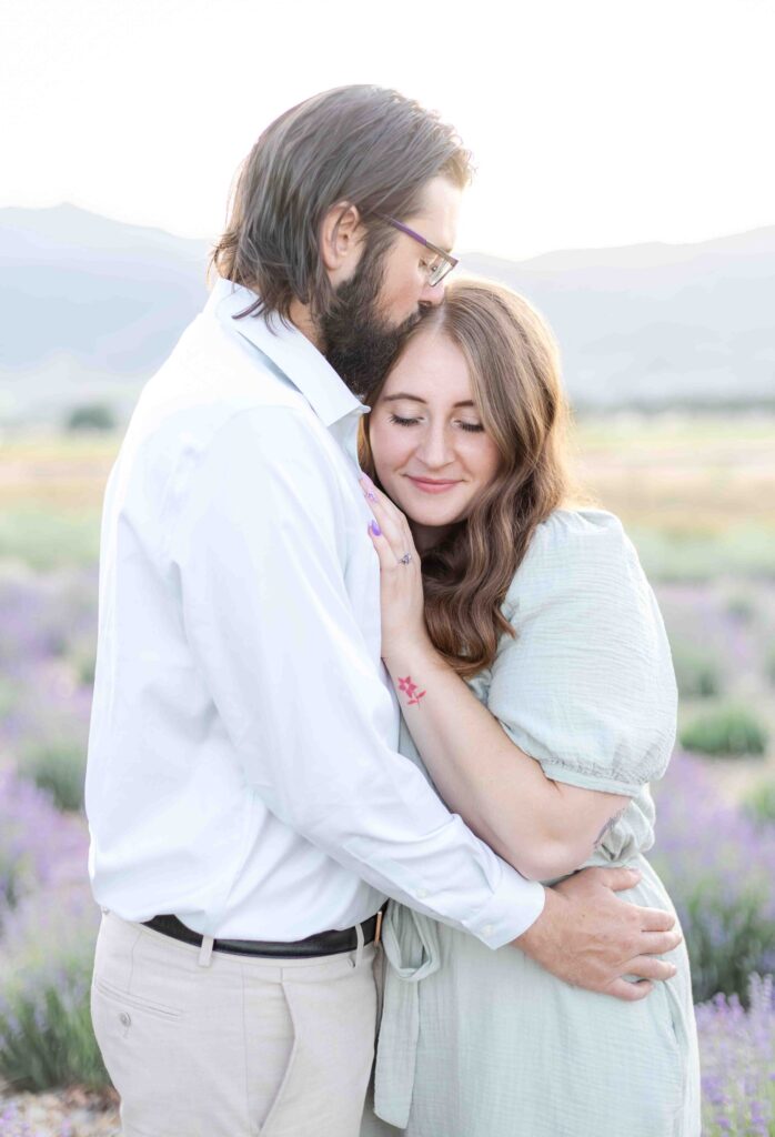 Engaged couple standing close together in a blooming lavender field during a sunset engagement session in Utah