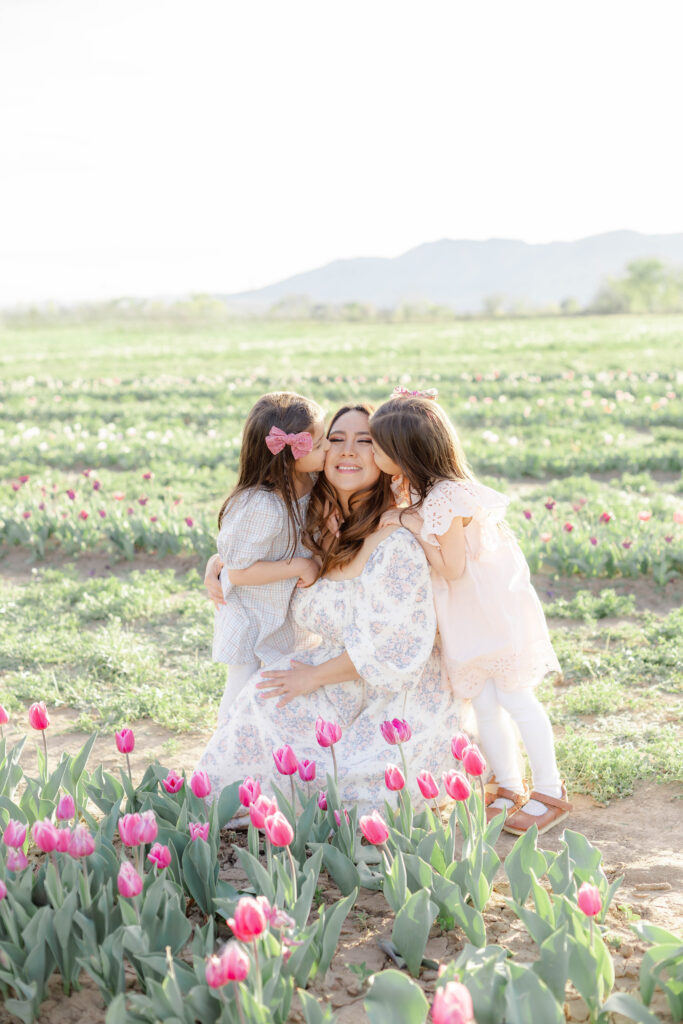 Twin girls kiss their mom on the cheeks among beautiful tulip blooms in Utah