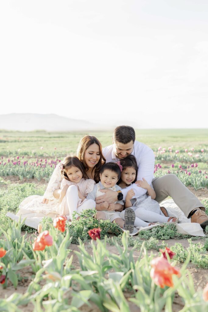 Parents hug their kids close while sitting on a blanket in a field of tulips in Utah