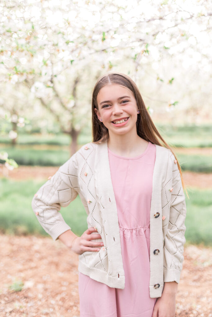 Young girl posing for a portrait in a Utah orchard surrounded by blossoming orchard trees and natural light.