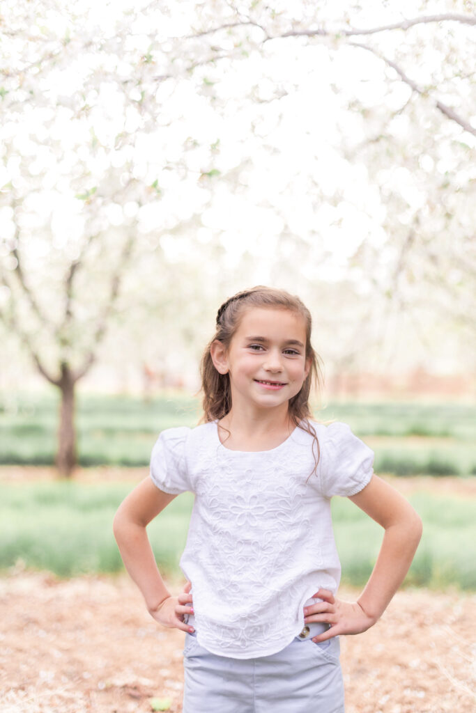 Little girl photographed in a blooming Utah orchard during a relaxed orchard family portrait session.