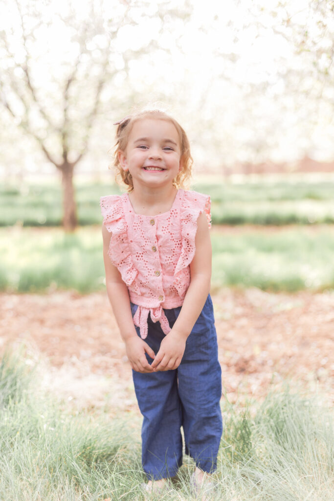 Little girl smiling in a Utah orchard, photographed in natural light during a Utah County family photo session in an orchard.