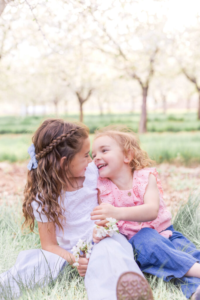 Two young girls laughing together in a Utah orchard during a family photo session.