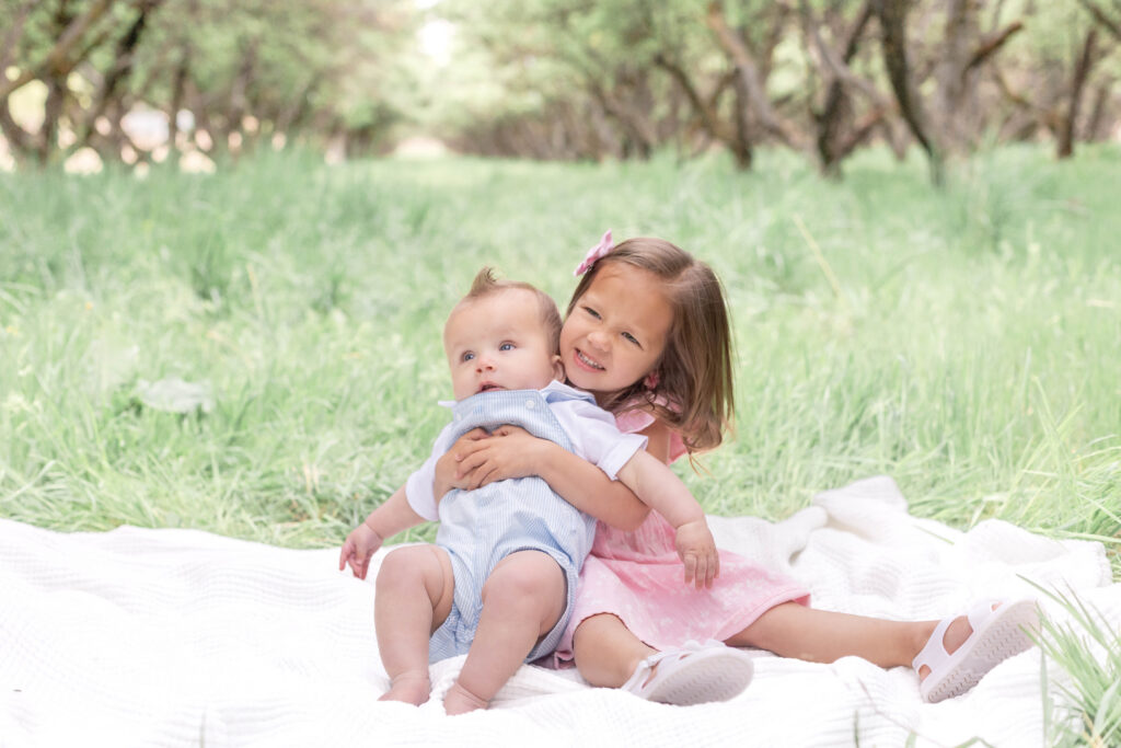 Candid spring family photography session in a Utah orchard of older sister holding baby brother