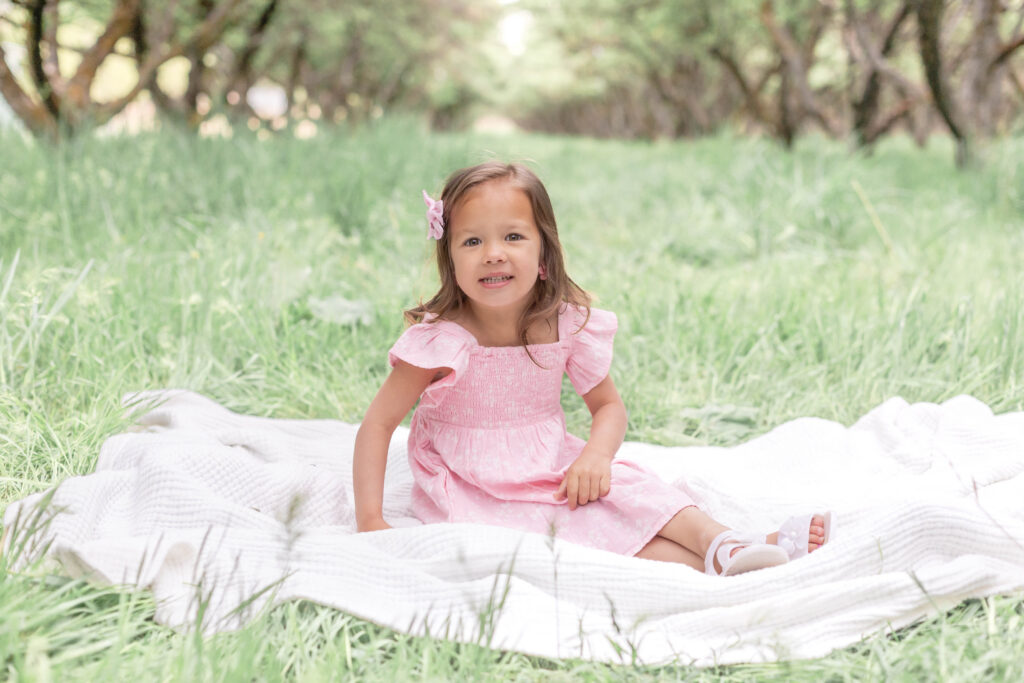 A cute little girl smiles in a Utah County orchard family photo session.