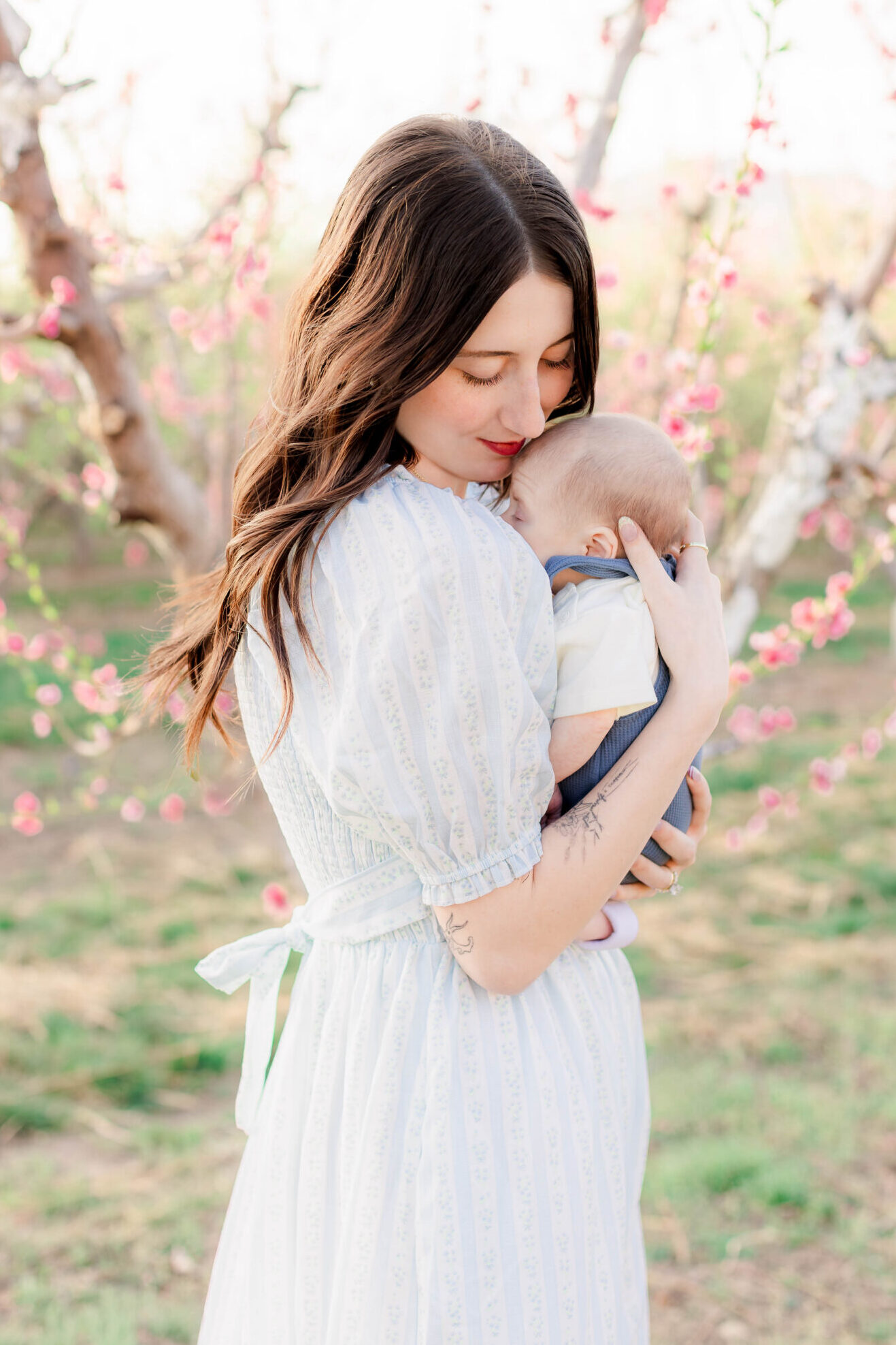 Mother holding her newborn baby in a blooming orchard in Utah during a soft and light-filled spring family photography session